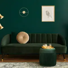 Elegancki salon z butelkową zielenią ściany. Miękka sofa, złota lampa i dekoracje tworzą przytulną atmosferę.
