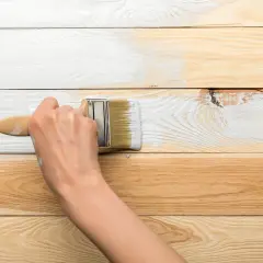 Ręka maluje białą farbą drewnianą boazerię, pokazując, jak odnowić boazerię lakierowaną.