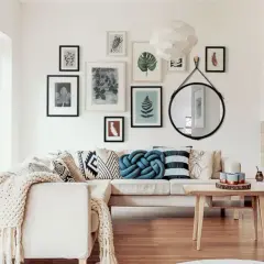 Salonowe lustro w czarnej ramie, galeria roślinnych grafik i przytulna kanapa. Inspiracje na stylowe wnętrze.