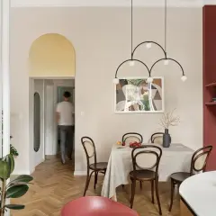 Złote łuki na ścianie dodają elegancji wnętrzu. W jadalni stół nakryty obrusem, krzesła z rattanu, a nad nimi nowoczesna lampa.
