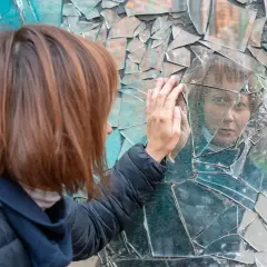 Kobieta dotyka rozbitego lustra, zastanawiając się, ile lat nieszczęścia po zbiciu lustra przyniesie jej ta sytuacja.