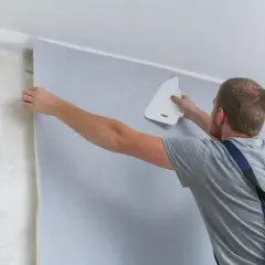 Mężczyzna pokazuje, jak się klei tapetę, wygładzając ją pacą.