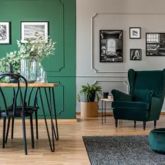 Elegancki salon z dominującym kolorem ścian butelkowa zieleń. Wygodny fotel i puf w tym samym odcieniu.