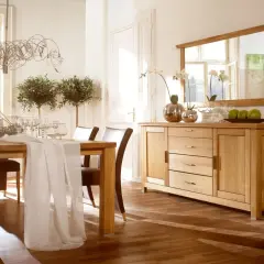Elegancka jadalnia z drewnianym stołem, krzesłami i komodą. Nad komodą wisi duże lustro, które odbija światło i okna.