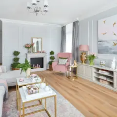 Przytulny pokój w odcieniach pudrowego różu i szarości. Miękka kanapa, różowy fotel i eleganckie meble tworzą harmonijną całość.