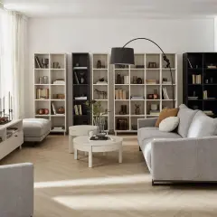 Przytulny szaro beżowy salon z sofą, regałami pełnymi książek i dekoracji, stolikami kawowymi i lampą.