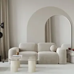 Nowoczesny salon z łukiem w tle. Beżowa kanapa, szklany stolik i lustro w łukowatej ramie tworzą stylowe inspiracje.