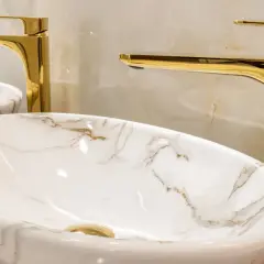 Elegancka łazienka z marmurowymi umywalkami i lśniącymi, złotymi dodatkami.