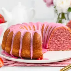 Różowy lukier na babce ucieranej, z jakich kolorów powstaje różowy? Obok świeże truskawki i sos.