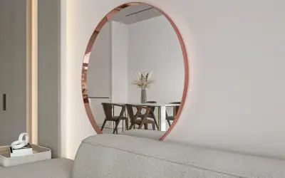 Okrągłe lustro w miedzianej ramie odbija elegancką jadalnię z drewnianymi krzesłami i wazonem z suszonymi kwiatami.