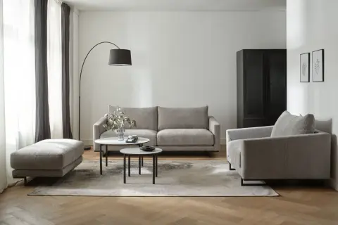 Nowoczesny salon z szarymi meblami i dywanem. W tle czarna szafa i zasłony w odcieniach szarości.