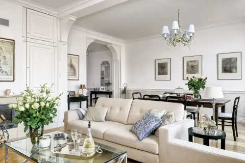 Eleganckie wnętrza w stylu hampton: jasna kanapa, szklany stolik z szampanem, bukiet róż i stylowe meble tworzą przytulną atmosferę.