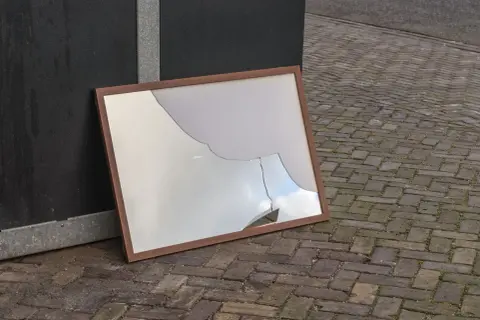 Zepsute lustro w drewnianej ramie leży na bruku. Czy lustro można wyrzucić do szkła?