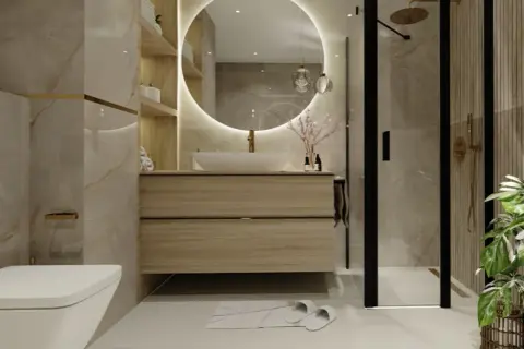 Elegancka łazienka z podświetlanym lustrem, nad którym znajduje się lampa nad lustro na baterie. Obok prysznic i toaleta.