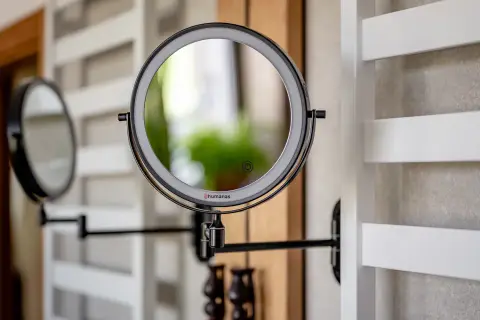 Eleganckie, czarne lustro łazienkowe z podświetleniem LED, zamontowane na wysięgniku. Obok widać drugie lustro.
