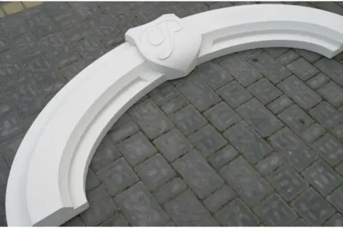Biały, ozdobny łuk nad drzwiami z herbem, gotowy do montażu. Idealny, by nadać wejściu elegancki charakter.
