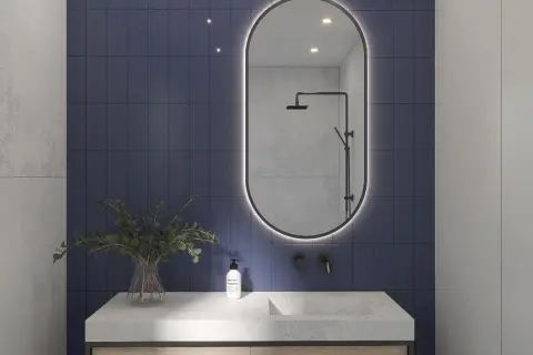 Eleganckie lustro z podświetleniem do łazienki nad kamiennym blatem z umywalką i roślinami.