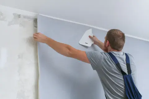 Mężczyzna pokazuje, jak się klei tapetę, wygładzając ją pacą.