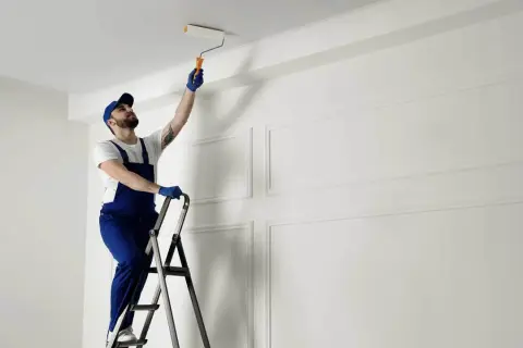 Malarz na drabinie odświeża sufit. Zastanawiasz się, co ile lat malować sufit? To zależy od materiału i warunków.