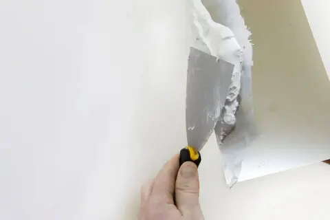 Dłoń z kielnią nakłada gips na białą ścianę.