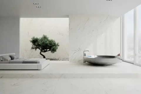 Nowoczesna łazienka z wanną i łóżkiem, gdzie króluje biały marmur. W tle drzewko bonsai.