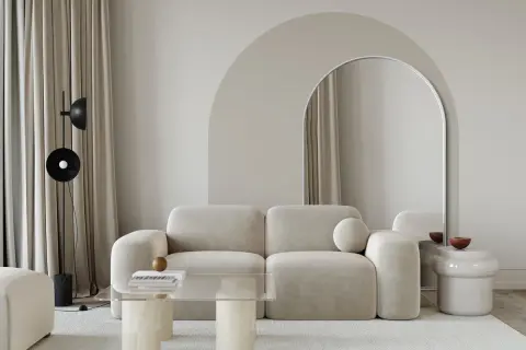 Nowoczesny salon z łukiem w tle. Beżowa kanapa, szklany stolik i lustro w łukowatej ramie tworzą stylowe inspiracje.