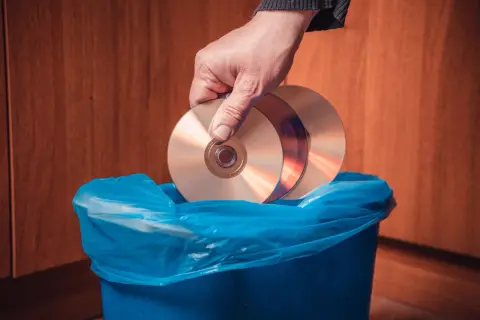 Dłoń wrzuca płyty CD do niebieskiego kosza. Zastanawiasz się, gdzie wyrzucić płyty GK?