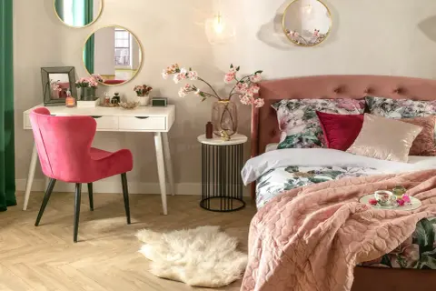 Elegancka toaletka w sypialni aranżacje: biała toaletka, różowe krzesło, lustra i kwiaty tworzą przytulną przestrzeń.