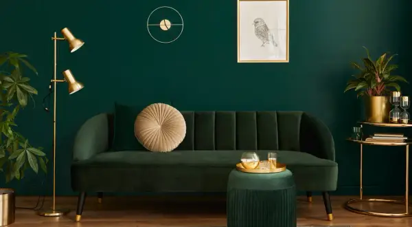 Elegancki salon z butelkową zielenią ściany. Miękka sofa, złota lampa i dekoracje tworzą przytulną atmosferę.