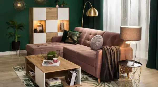 Elegancki salon z różowymi dodatkami do salonu: pikowana kanapa, stolik kawowy, dywan z motywem liści, złote dekoracje ścienne i lampa.