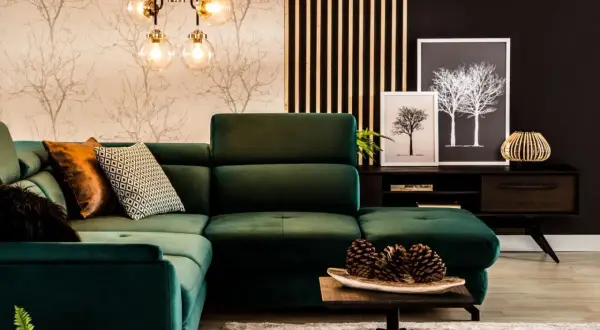 Wygodna, ciemno zielona kanapa w salonie z ozdobnymi poduszkami i lampą w stylu retro.