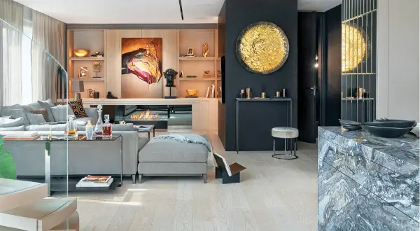Elegancki salon z kominkiem i sofą. W tle widać półki z dekoracjami, a po prawej stronie lustrzana ściana w salonie odbija złoty dysk.