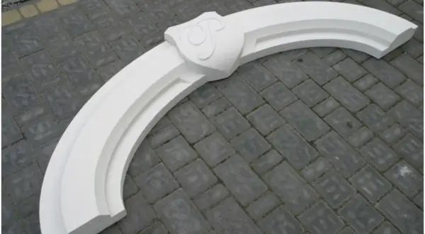 Biały, ozdobny łuk nad drzwiami z herbem, gotowy do montażu. Idealny, by nadać wejściu elegancki charakter.