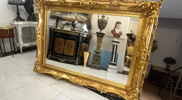 Wspaniałe lustro w bogatej, złotej ramie, odbijające antyczne meble i dekoracje.