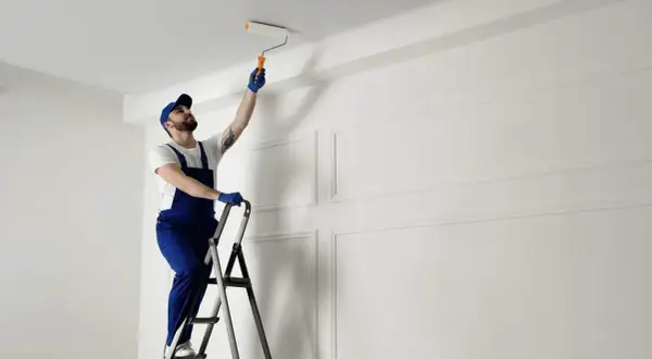 Malarz na drabinie odświeża sufit. Zastanawiasz się, co ile lat malować sufit? To zależy od materiału i warunków.