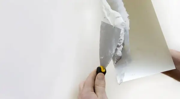 Dłoń z kielnią nakłada gips na białą ścianę.