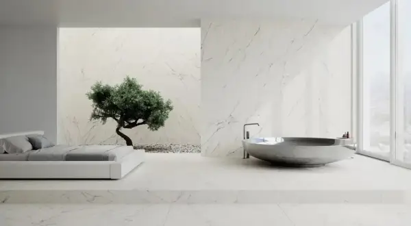 Nowoczesna łazienka z wanną i łóżkiem, gdzie króluje biały marmur. W tle drzewko bonsai.