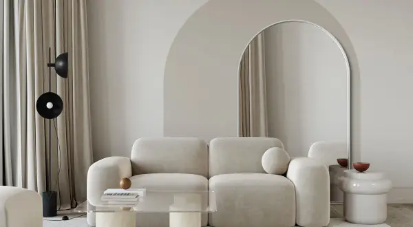Nowoczesny salon z łukiem w tle. Beżowa kanapa, szklany stolik i lustro w łukowatej ramie tworzą stylowe inspiracje.