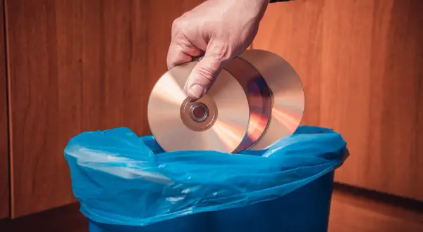 Dłoń wrzuca płyty CD do niebieskiego kosza. Zastanawiasz się, gdzie wyrzucić płyty GK?