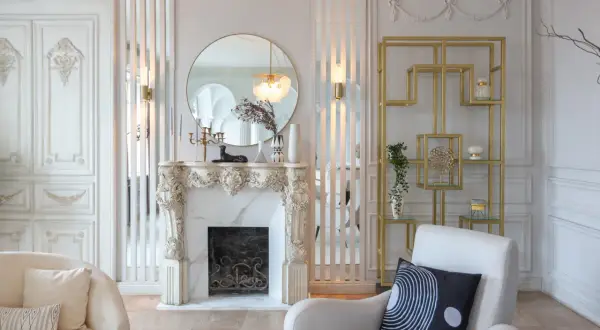 Elegancka ściana glamour w salonie z marmurowym kominkiem, złotym regałem i okrągłym lustrem.