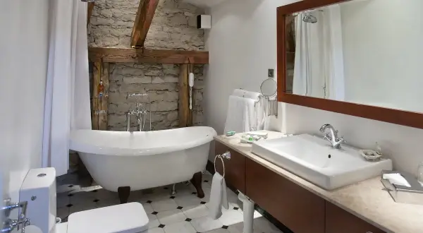 Łazienka z wanną wolnostojącą i kamienną ścianą. Duże lustro łazienkowe retro nad umywalką dodaje uroku.