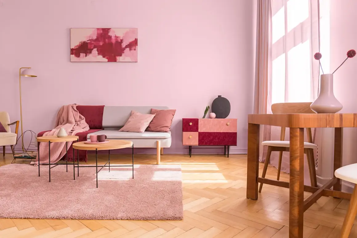 Przytulny salon z sofą, stolikami kawowymi i dywanem w odcieniach brudnego różu. Ściany w tym samym kolorze tworzą ciepłą atmosferę.