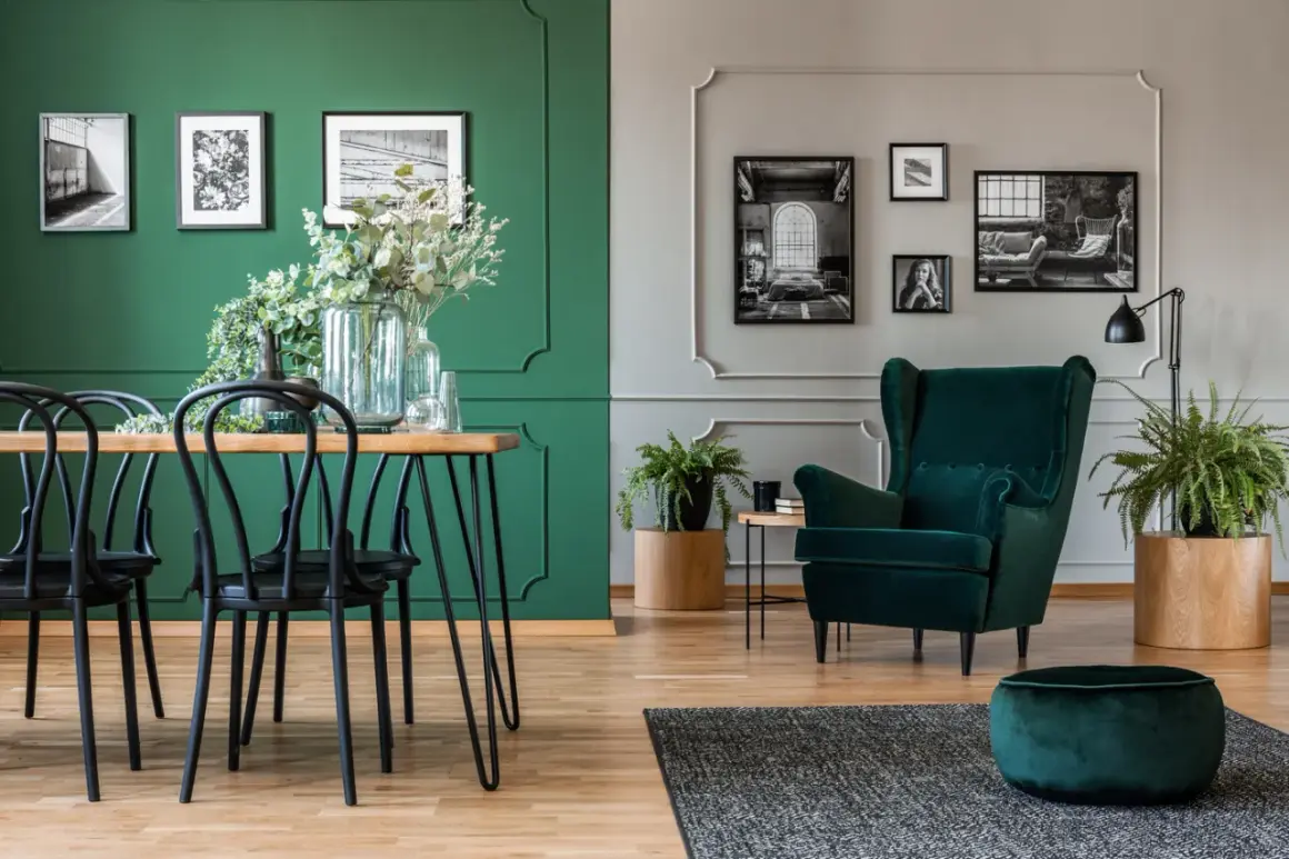 Elegancki salon z dominującym kolorem ścian butelkowa zieleń. Wygodny fotel i puf w tym samym odcieniu.