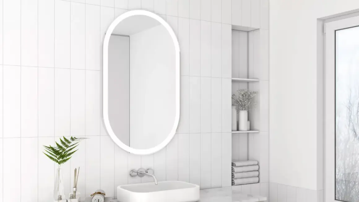 Owalne lustro z podświetleniem to idealne rozwiązanie, jakie lustro do małej łazienki. Minimalistyczny design, białe płytki i subtelne dodatki tworzą jasną przestrzeń.