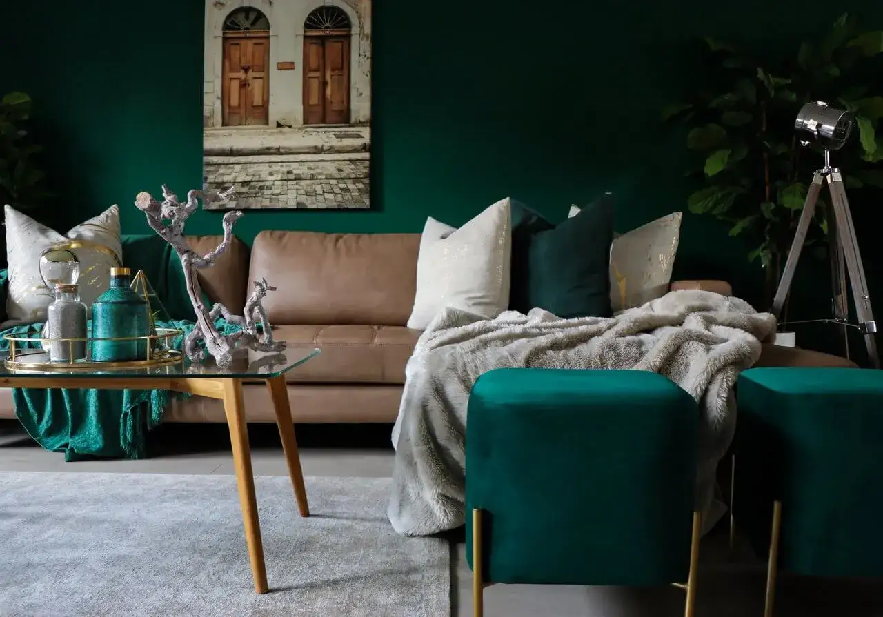 Elegancki salon z kanapą w kolorze karmelowym, poduszkami w odcieniach zieleni i złota, oraz pufami w kolorze zgniła zieleń.