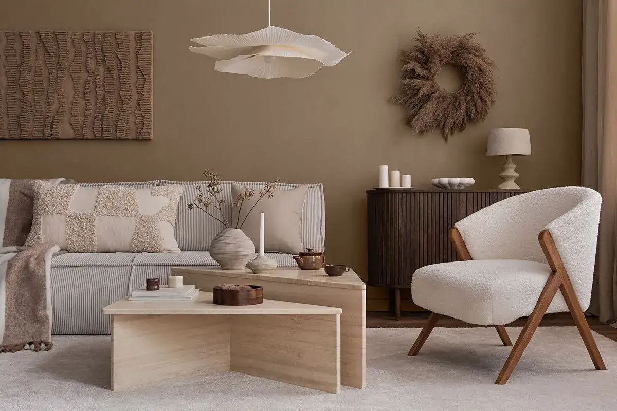 Przytulny salon w beżach i brązach. Miękka sofa, puszysty fotel i kamienne stoliki tworzą ciepłą atmosferę.