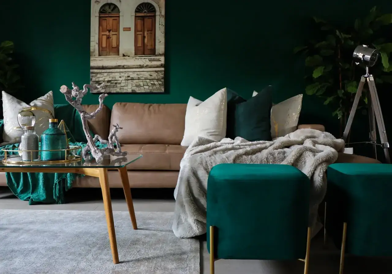 Elegancki salon z butelkową zielenią ściany, brązową kanapą, pluszowymi pufami i złotymi dodatkami.