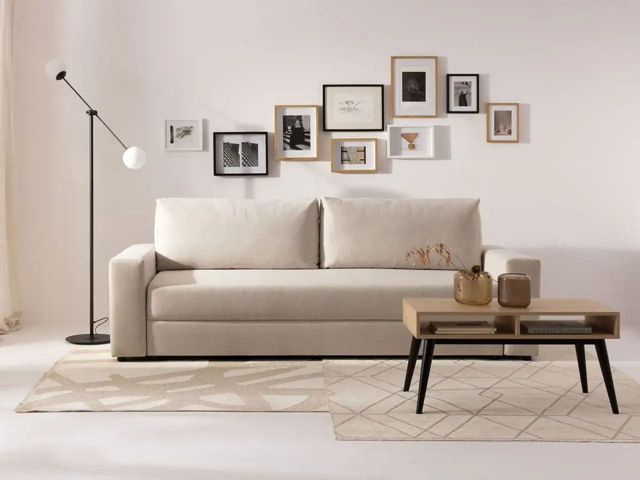 Przytulny salon w beżach i szarościach. Jasna kanapa, geometryczny dywan i galeria obrazów na ścianie tworzą harmonijną przestrzeń.