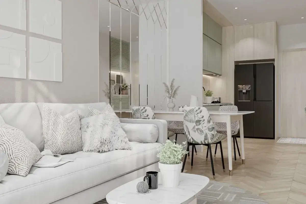 Przytulny salon w beżach i szarościach z wygodną sofą, stolikiem kawowym i jadalnią. W tle kuchnia z czarną lodówką.