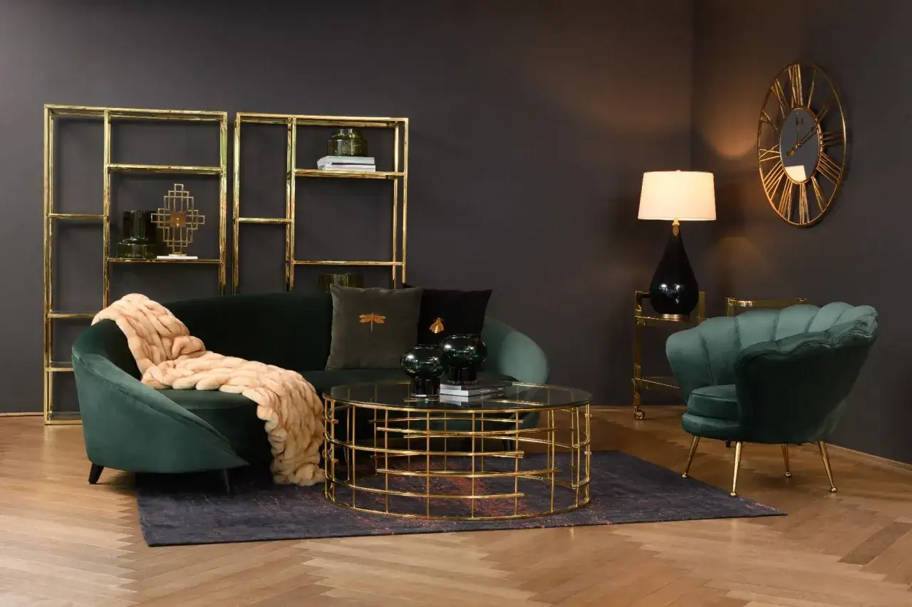 Elegancki salon z butelkową zielenią ścian, aksamitną kanapą i fotelem, złotymi regałami i stolikiem kawowym.